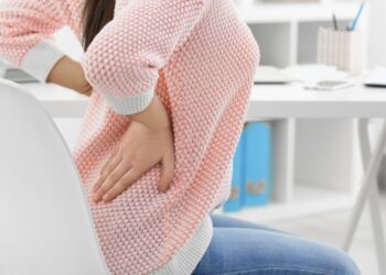 Beautiful young woman suffering from backache in office